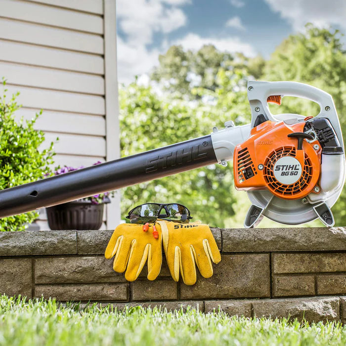 Stihl leaf blower on a stone ledge with yellow gloves and sunglasses, outdoor setting.