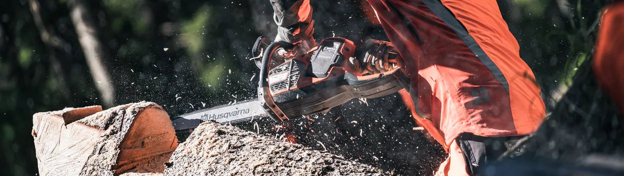 Person in orange safety gear using a chainsaw on a log with a forest background